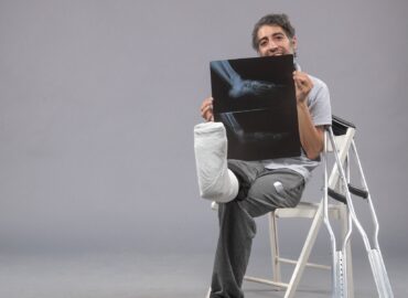 front view young male sitting with broken foot and holding x-ray of it on grey background pain leg broken male accident foot twist